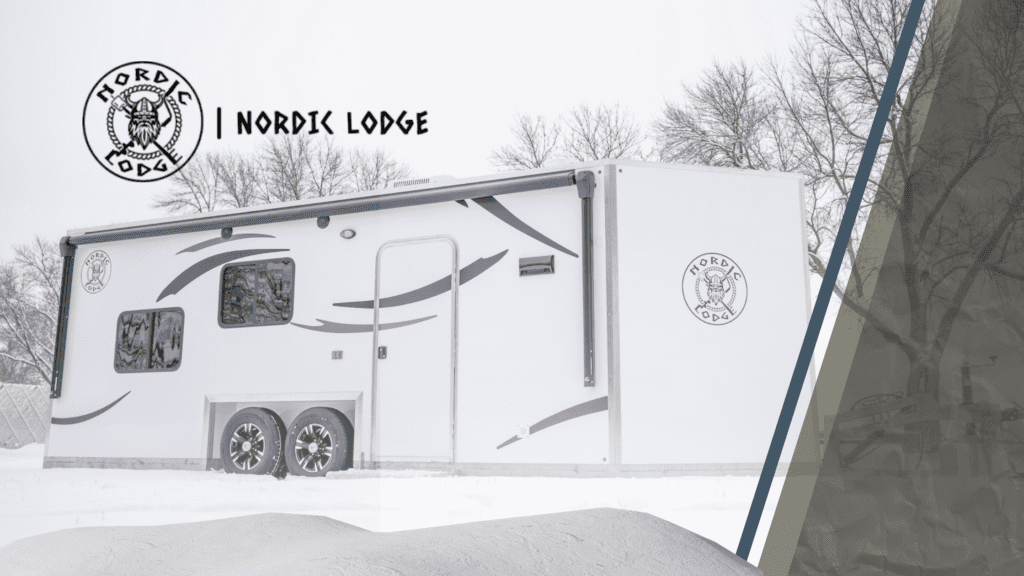 A Nordic Lodge camper in the snow with a snow drift in the foreground and the Nordic Lodge logo